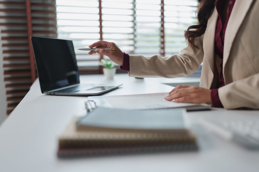 Mujer de negocios en su escritorio revisando documentos junto a una computadora portátil