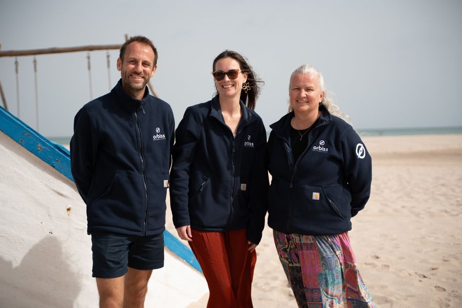 Tres integrantes del equipo de Orbiss con chaquetas de Orbiss en la playa