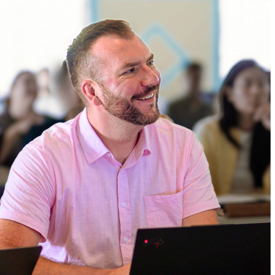 Orbiss team member in a pink shirt smiling at a laptop, with colleagues in the background