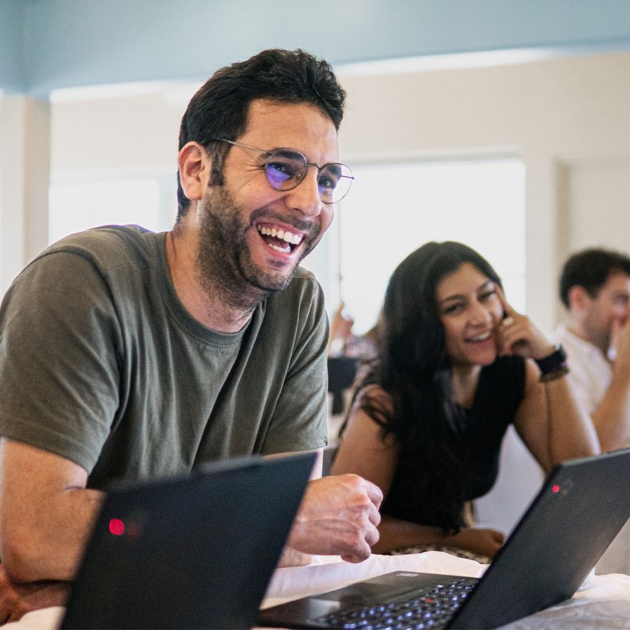 Orbiss team member in glasses laughing at a laptop, with colleagues smiling in the background