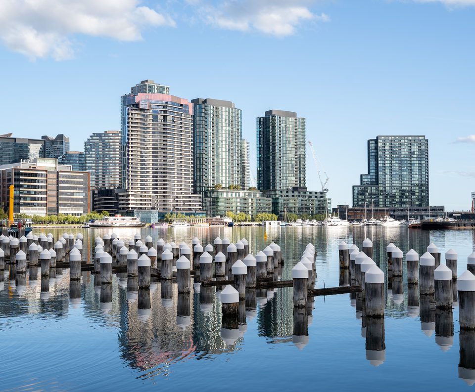 Melbourne waterfront towers reflected in still water behind old pier posts