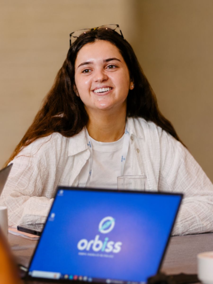 Integrante del equipo de Orbiss sonriente frente a una computadora portátil con el logo de Orbiss en pantalla