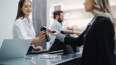 Une cliente paie avec son smartphone sur un terminal de paiement tendu par une caissière souriante