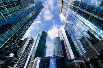 Looking up at glass skyscrapers reflecting a blue sky with white clouds