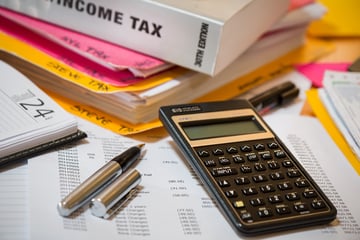 Calculator, pen and financial statements in front of an income tax book and colored folders